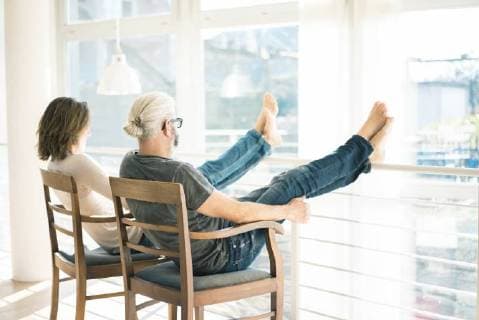 IMAGO Creative: Internationaler Frauenmonat, Gesundheit, Frauen in der Menopause Relaxed mature couple sitting on chairs at home with feet up model released Symbolfoto property released  MOEF00988