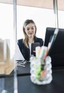 Smiling young businesswoman using cell phone at desk in office model released Symbolfoto property released  UUF13156