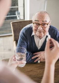 Woman holding pill and glass of water for smiling senior man model released Symbolfoto property released  UUF12905