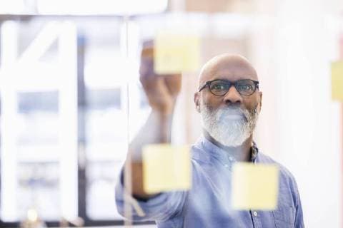 Portrait of businessman taking adhesive note from glass wall in office model released Symbolfoto property released  FMKF04931