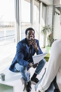 Smiling businessman with papers sitting at the window meeting colleague model released Symbolfoto property released  UUF13101