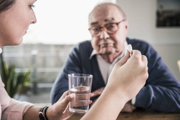 Woman holding pill and glass of water for senior man model released Symbolfoto property released  UUF12904