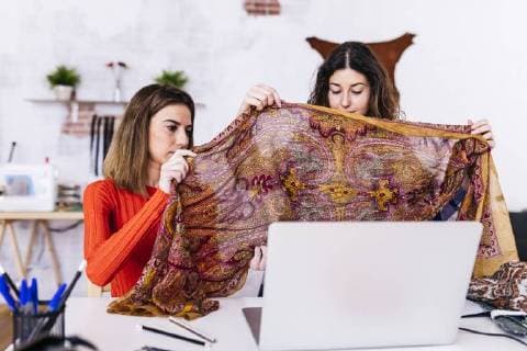 Two fashion designers in studio with laptop examining fabric model released Symbolfoto property released  JRFF01588