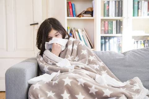 Sick girl sitting on the couch at home blowing nose model released Symbolfoto  LVF06797