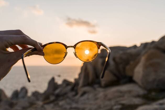IMAGO Creative, Jahreszeit Sommer, Sonnenschutz Man s hand holding sunglasses in front of evening sun, close-up model released Symbolfoto  AFVF00411