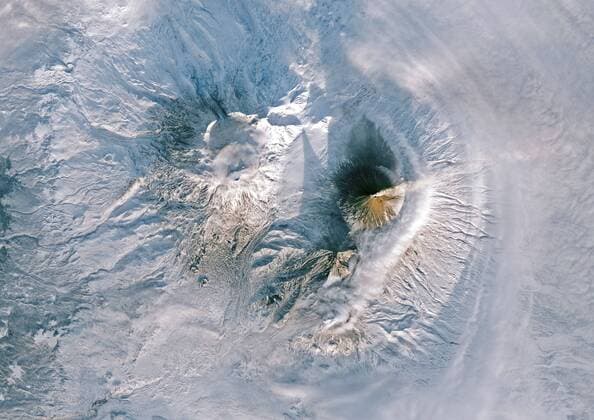 Color satellite image of Volcanoes on Kamchatka Peninsula, Russia. Klyuchevskaya, to the right, the tallest and most active volcano on the peninsula is emitting a small plume of gas, steam, and ash. Strecthing along the northwest rim of the Pacific Ring of Fire, Kamchatka is one of the most volcanically active regions in the world. Image collected on January 10, 2018. 913_03_PO07683