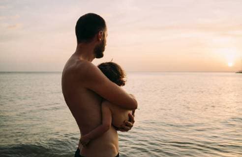 IMAGO Creative: Vaterschaft Father holding little daughter on his arms while watching sunset together at the sea model released Symbolfoto  GEMF01975