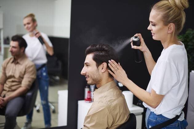Smiling hairdresser using hairspray on man s hair model released Symbolfoto property released  ABIF00353