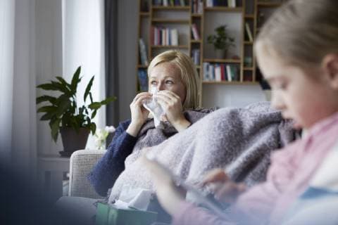 Mother sitting on couch, having a cold, daughter playing in foreground model released Symbolfoto property released  RBF06276