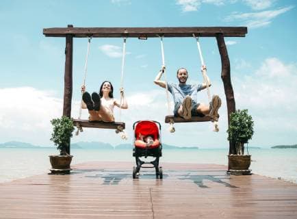 Thailand, Koh Lanta, happy parents on wooden swings in front of the sea and sleeping baby in a stroller model released Symbolfoto  GEMF02047