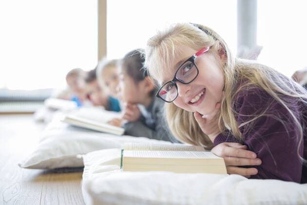 Portrait of smiling schoolgirl lying on the floor with classmates reading book in school break room model released Symbolfoto property released  WESTF24160