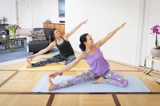 An image of two women doing yoga in the living room at home