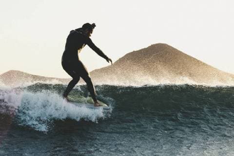 Side view shot of longboard surfer in wetsuit riding wave in sea at sunset, Tenerife Canary Islands Spain VISE003738 model released Symbolfoto Copyright: SergioxVillalba VISE003738