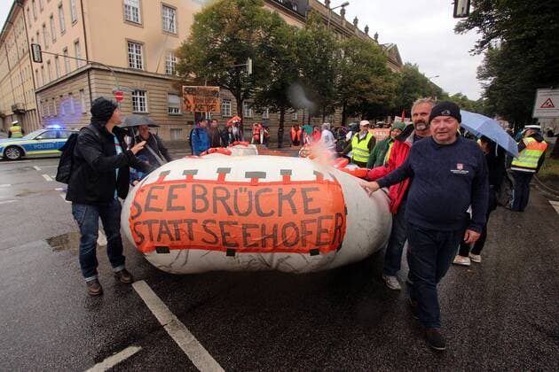 Demonstration Seebrücke Brücken statt Mauern gegen die Politik der Abschottung der EU Europäische n Union durch das Schikanieren von Hilfsschiffen und Organisationen der Flüchtlingshilfe und dem daraus resultierenden Massensterben von Flüchtlingen auf dem Mittelmeer in München, Bayern, Deutschland. Rettungsboot mit Aufschrift Seebrücke statt Seehofer bildet die Spitze des Demonstrationszug es. Der Kapitän des festgesetzten Seenotrettungsschiff s Mission Lifeline, Claus-Peter Reisch, hilft mit beim Ziehen des Bootes (vorne rechts)