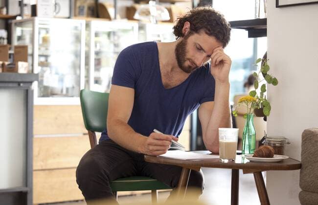 Pensive young man sitting in a coffee shop writing letter model released Symbolfoto property released  MFRF00913