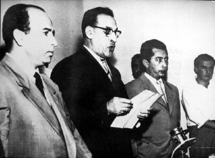 FERHAT ABBAS (C)) , PRESIDENT OF THE PROVISIONAL GOUVERNMENT OF THE ALGERIAN REPUBLIC SEEN READING IN FRONT OF SEVERAL JOURNALISTS, IN TUNIS, DURING WHICH HE IS DISPOSED SENDING A DELEGATION TO PARIS TO MEET GENERAL DE GAULLE. AT L: KRIM BELKACEM, VICE PRESIDENTOF THE GPRA, AND AT RIGHT BEN TOBBAL , INTERIOR MINISTER. .JEP.  x402113x