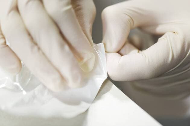 Healthcare worker wearing latex gloves, opening sterile package containing medical supplies  Copyright: OdilonxDimier B75994308