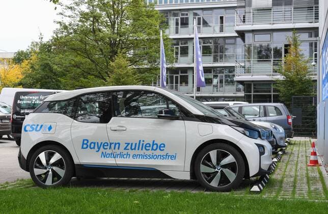 Ein Elektrofahrzeug mit dem Schriftzug: Bayern zuliebe- CSU steht an einer Ladestation E-Lade-station n und Schriftzug am Franz Josef Strauss- Haus, der CSU-Zentrale in München.