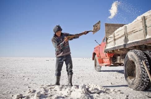 SALAR DE UYUNI, UYUNI, BOLIVIA. A Bolivian man in a wool sweater and rubber boots shovels salt from a flat desert scene into the flat bed of an old red truck. The Uyuni salt flat holds one of the world s largest reserves of lithium., Uyuni Bolivia Copyright: DavidxHanson 4521700009