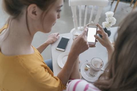 Two girlfriends meeting in a coffee shop, using smartphone model released Symbolfoto property released  JOSF02386