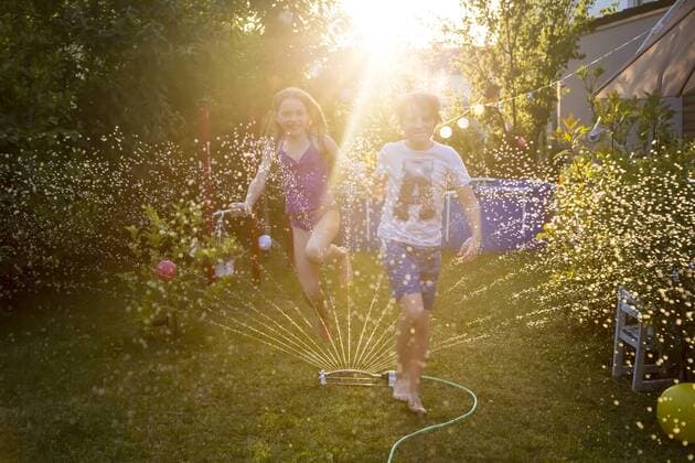 Brother and sister having fun with lawn sprinkler in the garden model released Symbolfoto property released  SARF03349