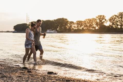 IMAGO Creative: Sommer, Abendspaziergang Happy young couple wading in river at sunset model released Symbolfoto  UUF11546