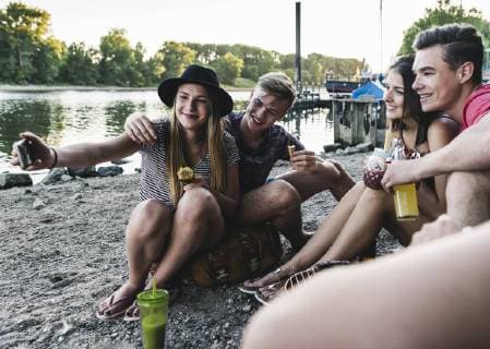 Group of friends sitting together having a barbecue and taking a selfie at the riverside model released Symbolfoto  UUF14841