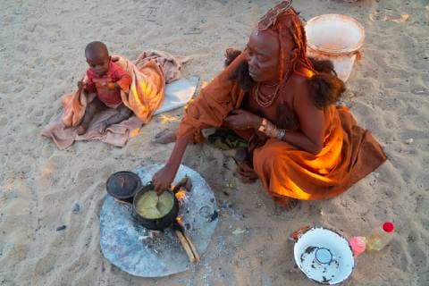 IMAGO Cultures of the world, Himba Volk in Namibia One senior red ochred Himba woman with her child cooking on an open fire, Puros Village, nearr Sesfontein, Namibia, Africa Copyright: JamesxStrachan 450-4365