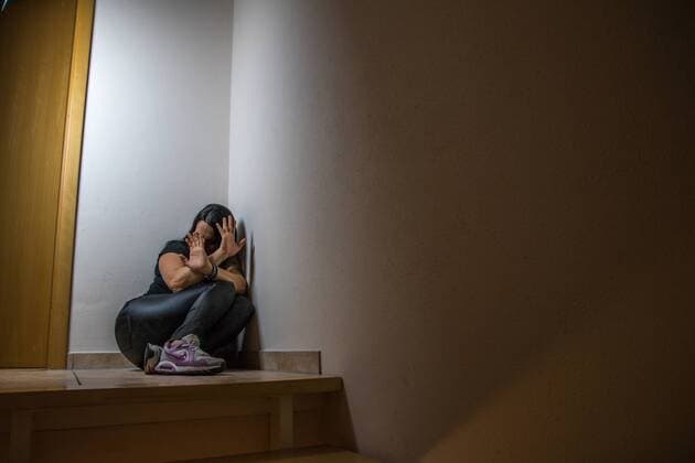 Junge dunkelhaarige Frau, zusammengekauert wehrt häusliche Gewalt mit Händen ab (Symbolbild) Häusliche Gewalt gegen Frauen - Symbolfoto