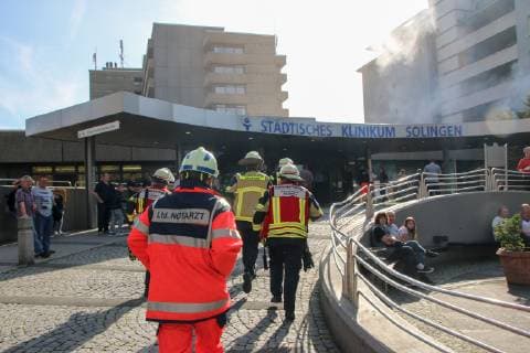 Rettungskräfte eilen zum Haupteingang des Städtischen Klinikum Solingen, im Hintergrund steigt simulierter Rauch aus einem der Patientenzimmer auf Bei einer Großübung im Klinikum Solingen erprobten insgesamt 450 Beteiligte ein Notfallszenario mit Brand und der Rettung von Patienten. Im 1. Obergeschoss des Hauses G des Klinikums Solingen brach simuliert ein Feuer aus welches sich ausbreitete. Großübung Klinikum Solingen, 06.10.18 Solingen NRW Deutschland Städtisches Klinikum *** Rescue workers rush to the main entrance of the Municipal Hospital Solingen in the background simulated smoke rises from one of the patient rooms In a large-scale exercise in the Solingen Hospital tested a total of 450 participants an emergency scenario with fire and the rescue of patients in the first floor of the house G of the hospital Solingen broke fire sim Copyright: xdnet_kwkx