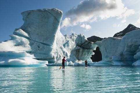 Two adults on stand up paddle board (SUP) observe hole melted in iceberg on Bear Lake in Kenai Fjords National Park, Alaska., Seward Alaska United States model released Symbolfoto Copyright: TurnerxForte FOJA000008