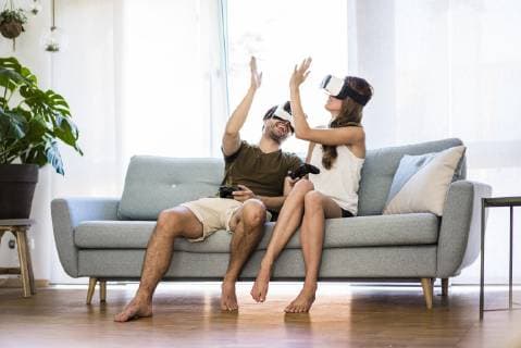 Happy couple sitting on couch at home wearing VR glasses high fiving model released Symbolfoto property released  JOSF02566