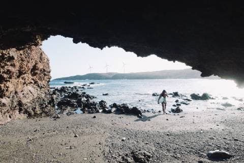 View from cave of female surfer in bikini walking with her surfboard on beach, Tenerife, Canary Islands, Spain, Tenerife Canary Islands Spain VISE004024 model released Symbolfoto Copyright: SergioxVillalba VISE004024