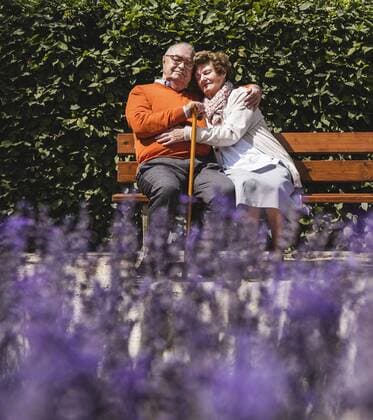 Senior couple sitting on bench in a park, with arms around model released Symbolfoto  UUF14934