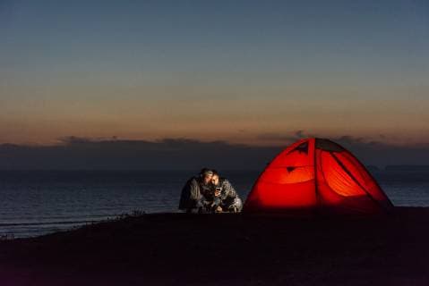 IMAGO Creative: Klimawandel - Nachhaltiges Reisen Romantic couple camping on the beach, using smartphone model released Symbolfoto  UUF15172