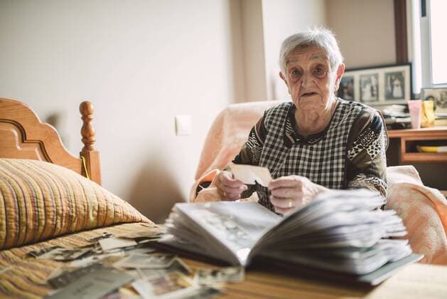Portrait of senior woman adding old photos to a photo album at home model released Symbolfoto property released  RAEF02217