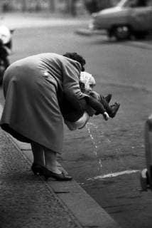 13.11.1965, Berlin, DDR - Frau haelt ihre Tochter zum Pullern am Bordstein ab. (30-40 Jahre, 60er Jahre, abhalten, Alltag, Alltagsleben, aussen, Aussenaufnahme, Berlin, bis 10 Jahre, Bordstein, DDR, deutsch, Deutsche Demokratische Republik, Deutschland, Elternteil, Erziehung, Europa, europaeisch, Familie, Frau, GDR, Generationen, Gesellschaft, halten, HF, historisch, Hochformat, Jahreszeit, Kaukasierin, kaukasisch, Kind, Kindererziehung, Kindheit, Kleinkind, Mama, Menschen, Mutter, Notdurft, Ost-Berlin, Ostberlin, Personen, pinkeln, pmscartandhistory, pullern, s w, schwarz weiss, schwarz-weiss, Schwarzweiss, Stadt, Stadtbild, Stadtleben, Strasse, Strassenrand, Strassenszene, Tochter, urinieren, Westeuropa, Winter, Wirtschaft, Zeitdokument, Zeitgeschichte) 651113KF418BERLIN.JPG *** 13 11 1965 Berlin GDR woman holds her daughter to pull pu
