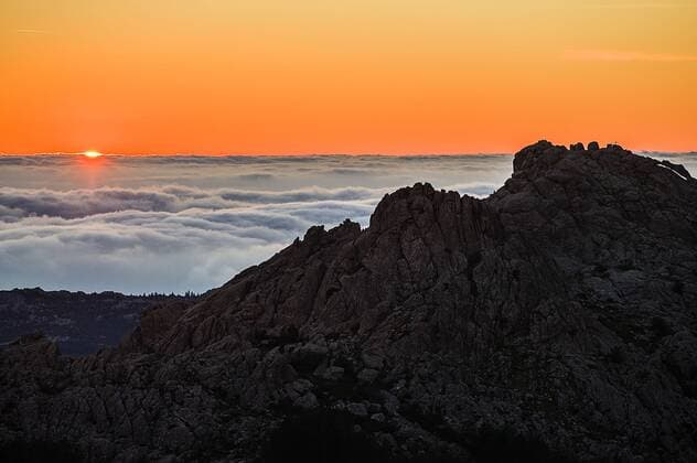 Panoramablick bei Sonnenuntergang über Felsen auf ein Wolkenmeer über der sardischen Gallura, Punta Balestrieri, Monte Limbara, Tempio Pausania Sardinien, Italien. Abendlicht auf dem Monte Limbara