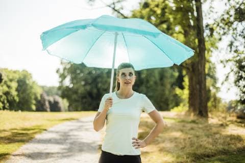 IMAGO Creative, Jahreszeit Sommer, Sonnenschutz Sportive young woman standing in a park holding sunshade model released Symbolfoto  MOEF01546