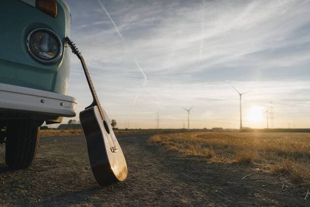 Guitar leaning against camper van in rural landscape with wind turbines at sunset  GUSF01404