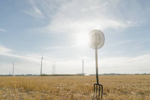IMAGO Creative: Landleben, Mit Nachhaltigkeit grün auf dem Land leben Pitchfork in field in rural landscape with wind turbines in background  GUSF01480