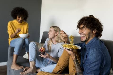 IMAGO Creative, Lifestyle, Leben in einer Wohngemeinschaft, WG Cheerful friends sitting on couch talking and eating model released Symbolfoto property released  VABF01887