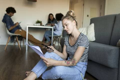 IMAGO Creative, Lifestyle, Leben in einer Wohngemeinschaft, WG Young woman sitting on floor with cell phone and papers and friends in background model released Symbolfoto property released  VABF01780