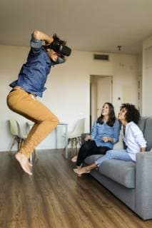IMAGO Creative, Lifestyle, Gaming Two women watching man with VR glasses jumping at home model released Symbolfoto property released  VABF01792