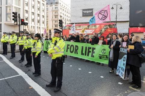 February 17, 2019 - London, Greater London, United Kingdom - Police officers stand in front of activists from Extinction Rebellion who disrupt London Fashion Week by stopping traffic and creating gridlock between the event venues on 17 February, 2019. Protesters call for the British Fashion Council to influence fashion industry to stop the trend of excessive consumption and unsustainable growth in the face of climate change and ecological collapse. Textiles production contributes 1.2 billion tonnes of carbon emissions annually and textiles are the largest single source (34.8%) of microplastic pollution affecting marine life. London United Kingdom  - ZUMAn230 20190217_zaa_n230_209 Copyright: xWiktorxSzymanowiczx