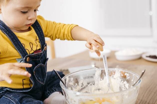 Toddler girl sitting on kitchen table throwing egg into bowl for preparing dough, partial view model released Symbolfoto property released  JRFF02337