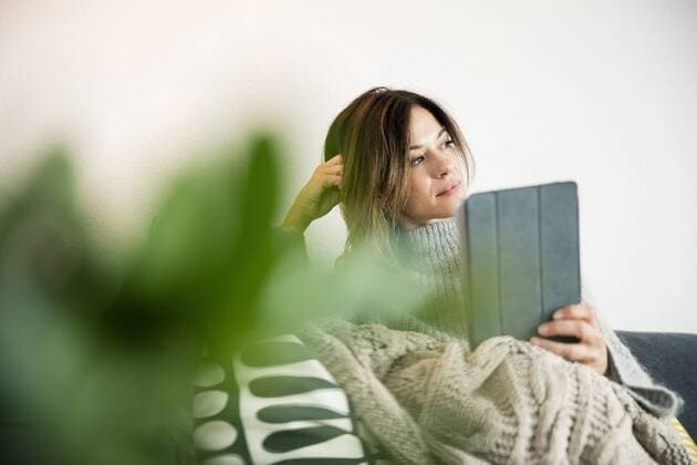 Woman sitting on couch, wrapped in a blanket, reading e-book model released Symbolfoto property released  MOEF01748