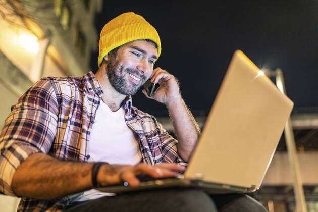 UK, London, smiling man using phone and laptop out in the city at night model released Symbolfoto  WPEF01226
