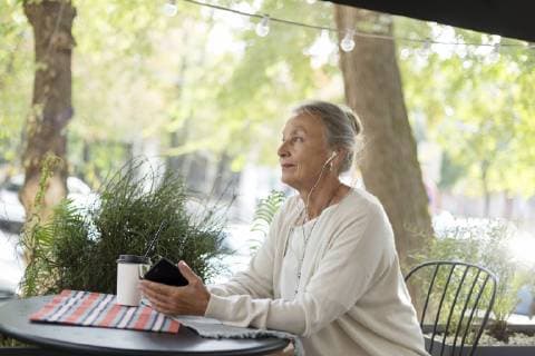 Senior woman at an outdoor cafe with cell phone and earphones model released Symbolfoto  VGF00056