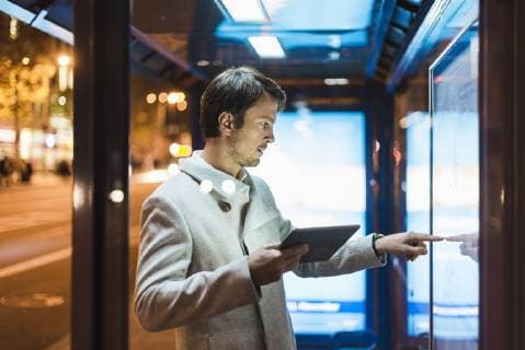 IMAGO Creative: Corporate: Klimaschutz, Digitalisierung und Urbanisierung Businessman with digital tablet standing at a bus stop at night model released Symbolfoto  DIGF05563